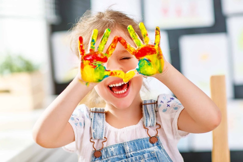 happy funny child girl draws laughing shows hands dirty with paint