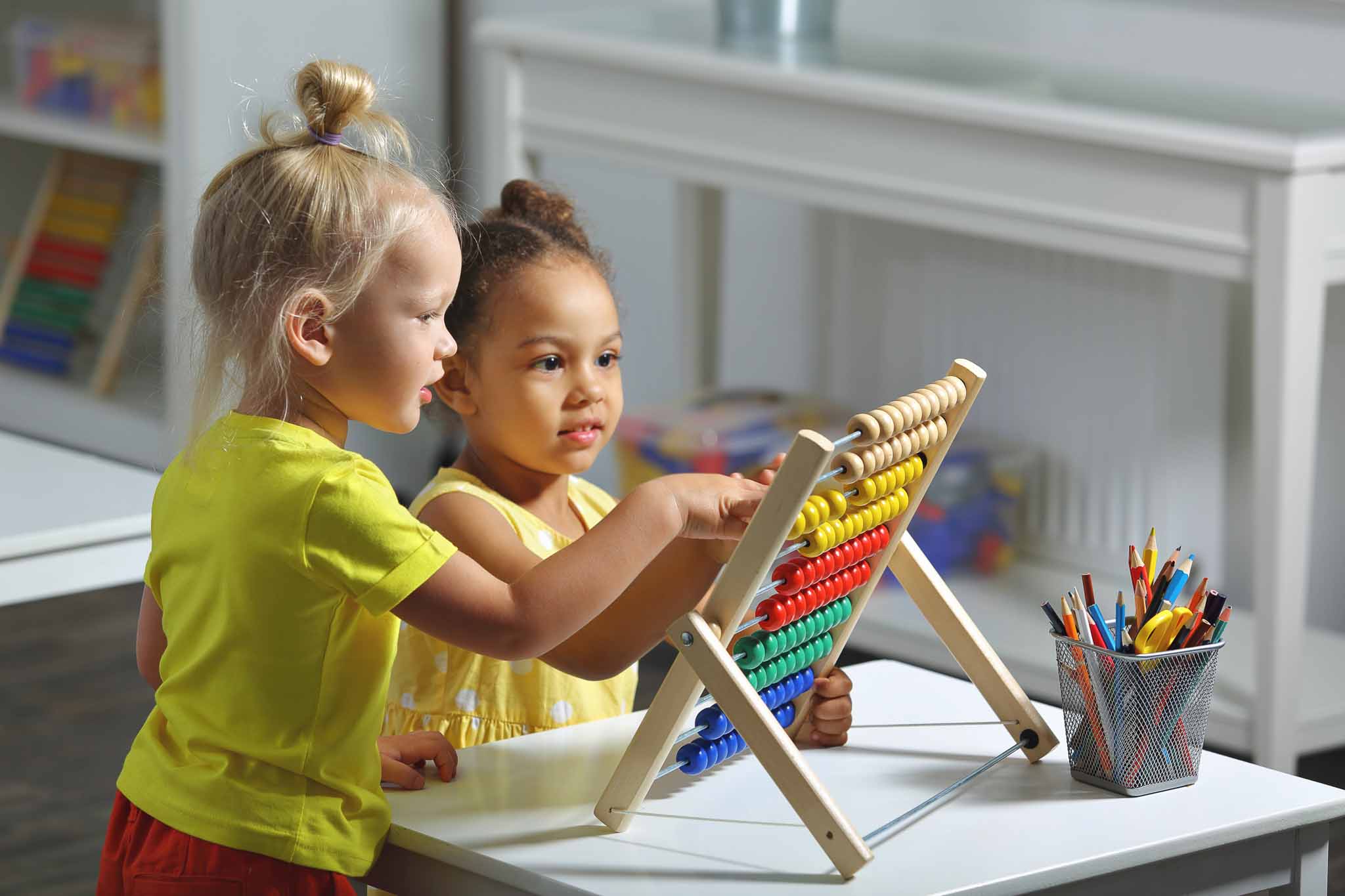 white and dark skinned children sit together at the table and count on the abacus and smiles