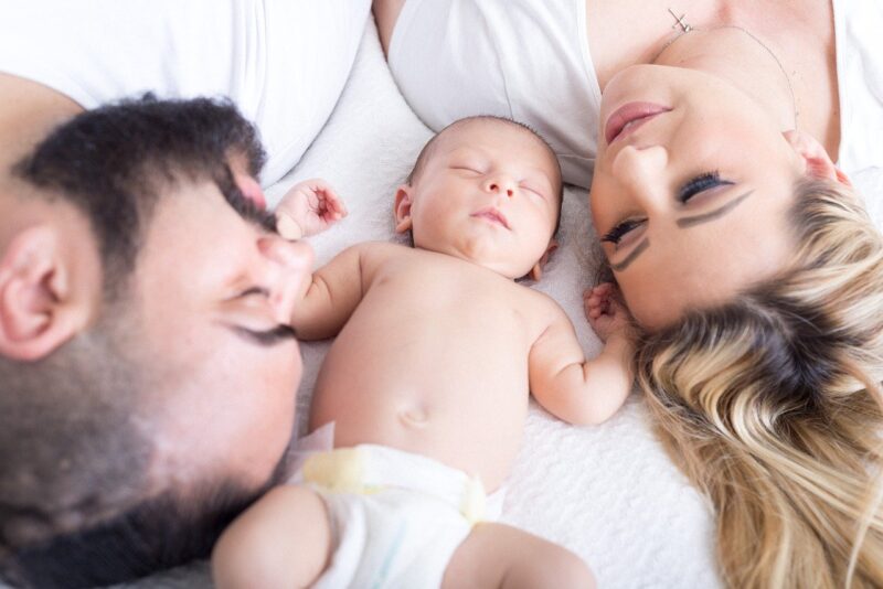 Newborn baby lying in bed between parents