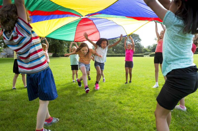 Half term summer kids camp - Children playing a game with a colourful Parachute
