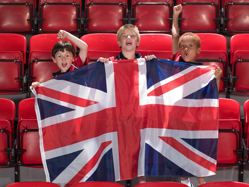 Boys cheering in an empty stadium holding the British Union Jack flat