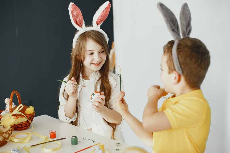 Children with bunny ears. Painted Easter eggs. Children with paints and brushes.
