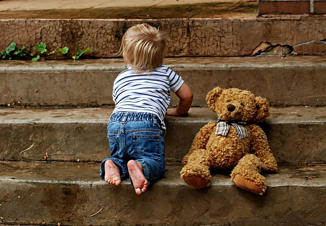 small boy crawling up steps with a teddy bear