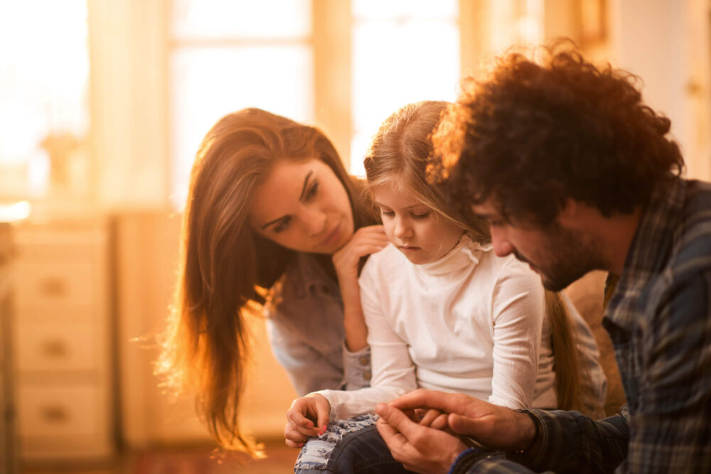 Sad little girl at home being consoled by her parents